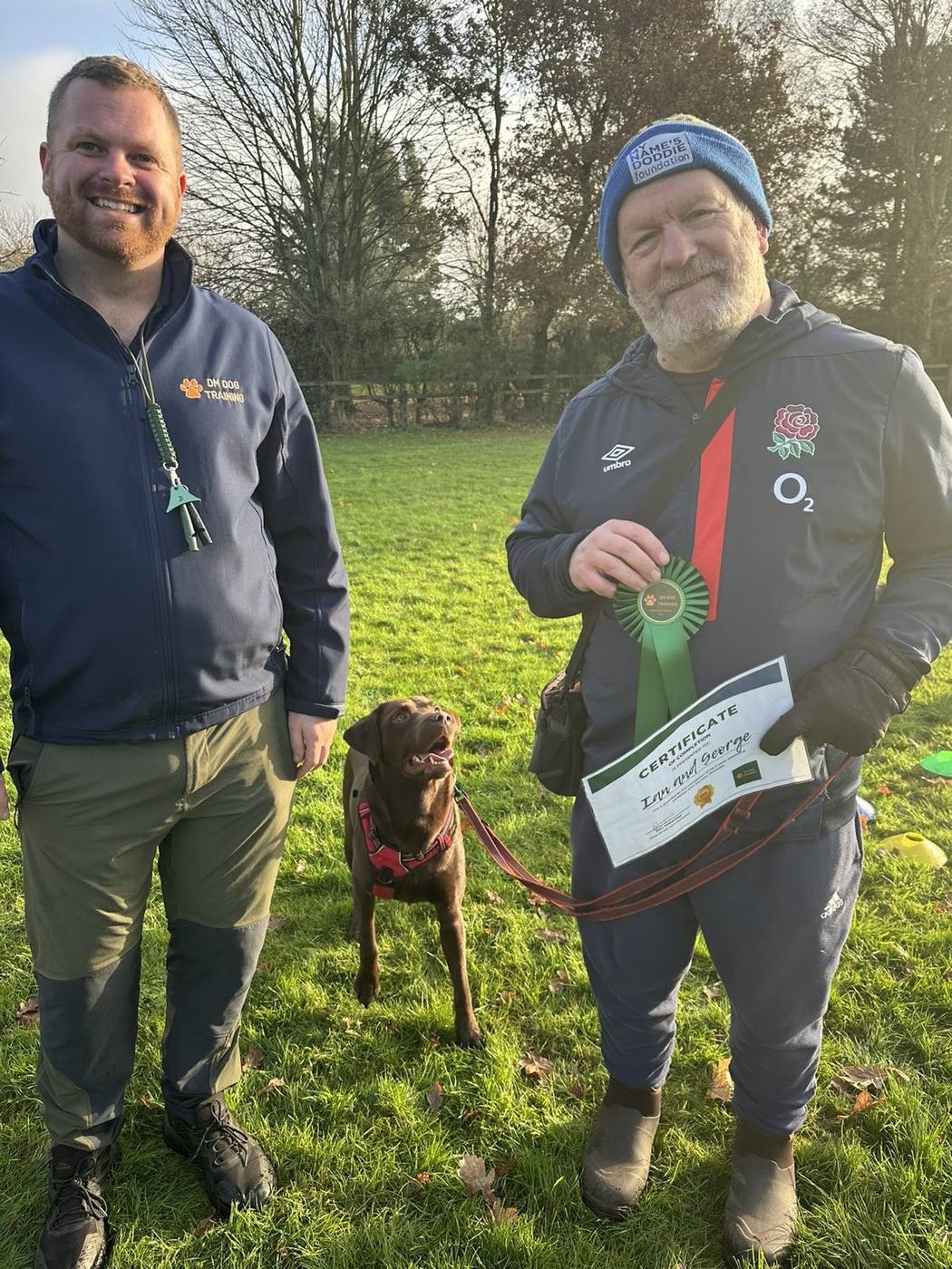 Dec with an owner and his chocolate Labrador, who is holding a course certificate and rosette