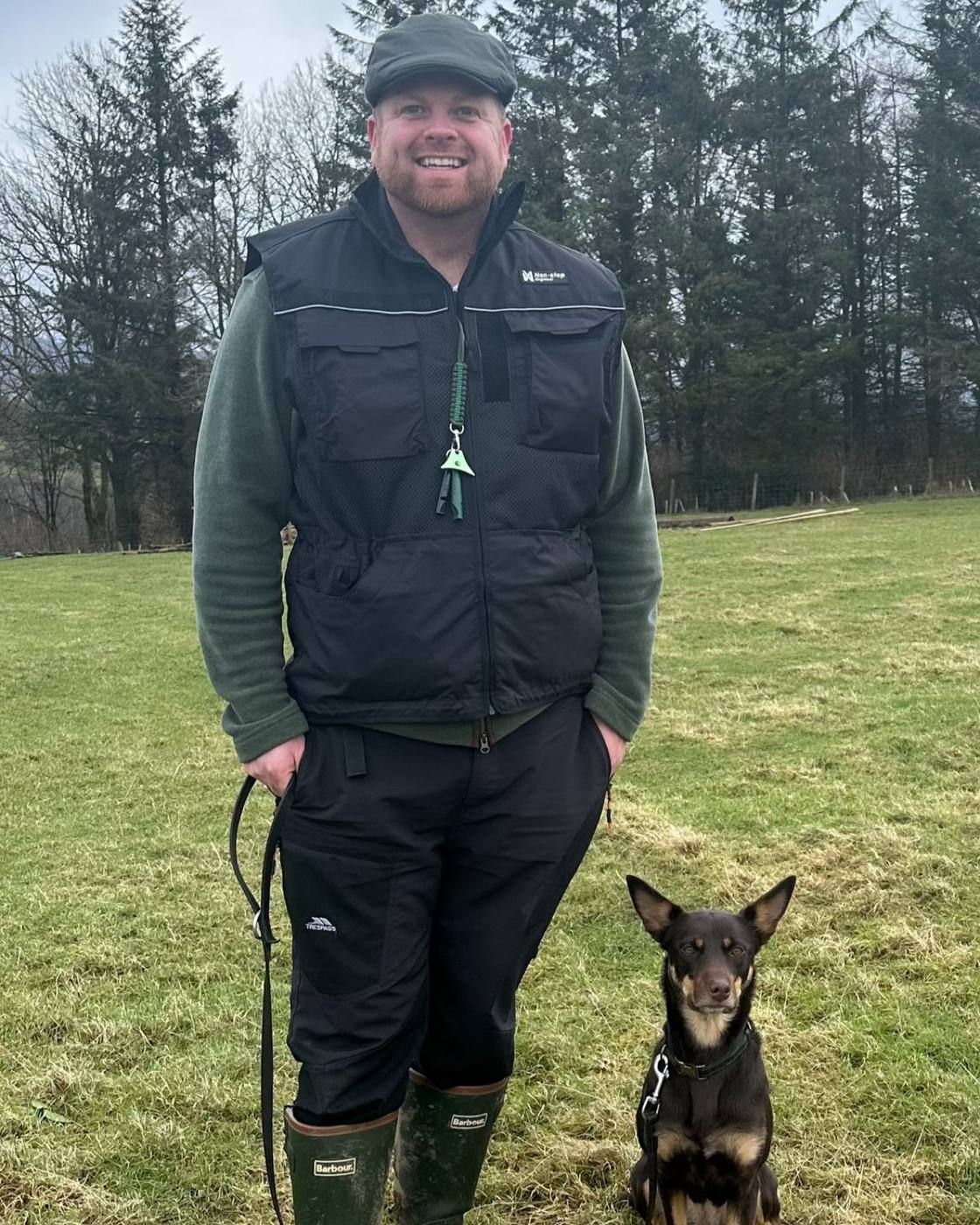 Dec Malarkey smiling in a field with a dog sitting beside him